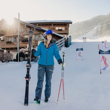Ski season opening days Woman in ski gear holding skis in front of chalet at sunny ski resort